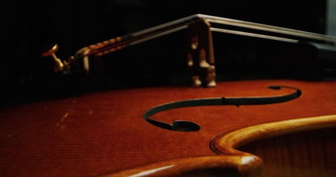 Slow motion artistic macro of master artisan luthier playing with a bow on a handmade violin or cello. Shot in 8K. Concept of spiritual instrument, art, orchestra, passion for music, sound, precision