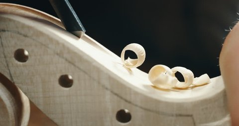 Slow motion macro of master artisan luthier painstaking detailed work on wood violin in a workshop. Shot in 8K. Concept of spiritual instrument, handmade, art, orchestra, artisan, passion for music
