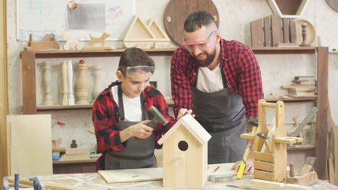 Time for family. Dad shows his little son how to make birdhouse in wooden workshop, using hand tools and wooden plank