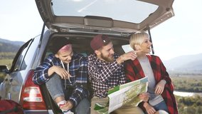 Happy hipster friends are looking at the road map while sitting in front of the travel car trunk with the smile. Friends inside a trunk car planning a road trip of mountains looking at a map, slow - Powered by Shutterstock - Get 15% off with code: PIKWIZARD15