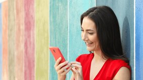 Excited woman checking smart phone content leaning in a colorful wall in the street