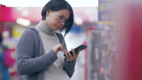 Side view close up of one pregnant Asian woman shopping in the supermarket,  looking at the mobile phone in hand searching for information,   pregnant female lifestyle using smartphone 4k clip 