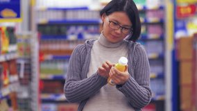 Front view of close up of one pregnant Asian woman shopping in the supermarket,  looking at one bottle of juice in hand reading, pregnant female lifestyle with smartphone 4k clip 