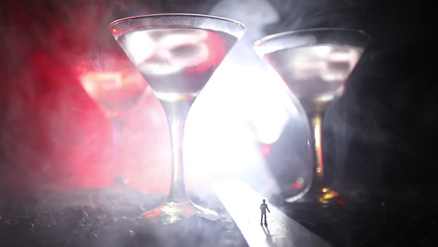 Abstract alcoholism concept. Silhouette of a man standing in the middle of the road on a misty night with giant glasses filled with alcoholic beverage. Creative artwork decoration