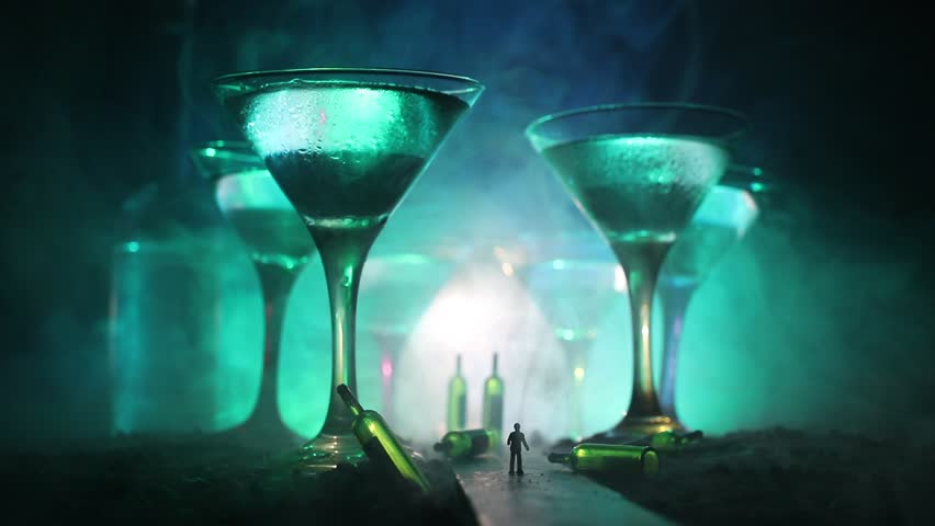 Abstract alcoholism concept. Silhouette of a man standing in the middle of the road on a misty night with giant glasses filled with alcoholic beverage. Creative artwork decoration