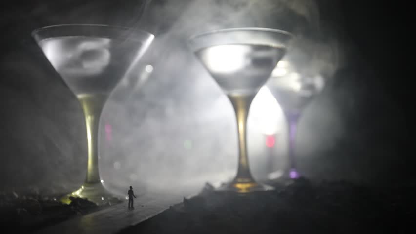 Abstract alcoholism concept. Silhouette of a man standing in the middle of the road on a misty night with giant glasses filled with alcoholic beverage. Creative artwork decoration