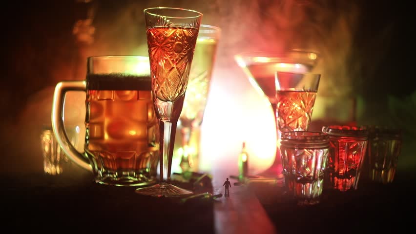 Abstract alcoholism concept. Silhouette of a man standing in the middle of the road on a misty night with giant glasses filled with alcoholic beverage. Creative artwork decoration