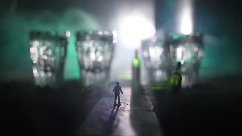 Abstract alcoholism concept. Silhouette of a man standing in the middle of the road on a misty night with giant glasses filled with alcoholic beverage. Creative artwork decoration