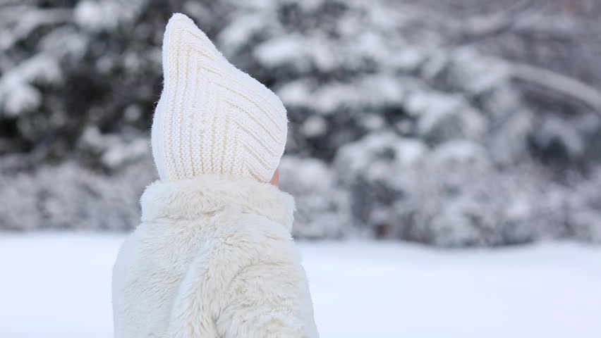 BACK VIEW: Portrait of little girl in white fur coat turns and pouts in the woods in winter