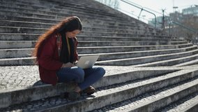 Thoughtful beautiful woman sitting on stairs with laptop on knees. Tired female student using laptop while sitting outdoor during sunny day. Overwork concept