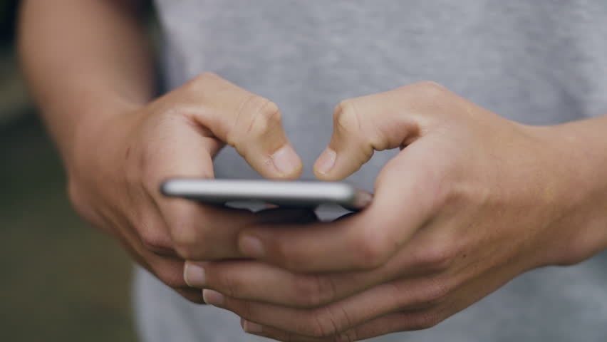 Front angle close up shot of a young male scrolling and typing on his phone outside Royalty-Free Stock Footage #1024656677