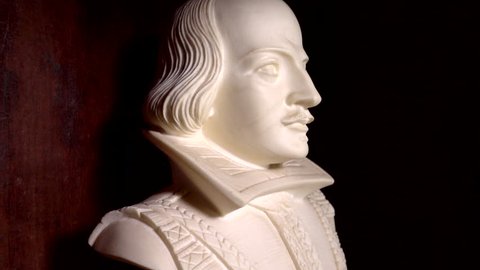 A slow motion close POV forward dolly shot of a Shakespeare bust on display in a wooden cabinet.