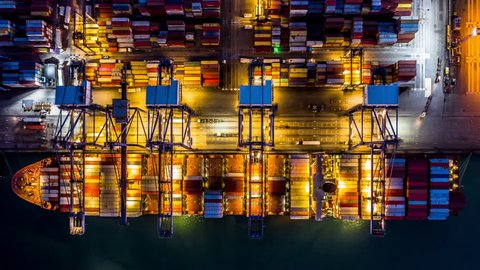 Time lapse 4K, Aerial top view Container cargo freight ship with working crane bridge discharge at container terminal, Business commercial container ship global at night, Freight shipment Singapore.