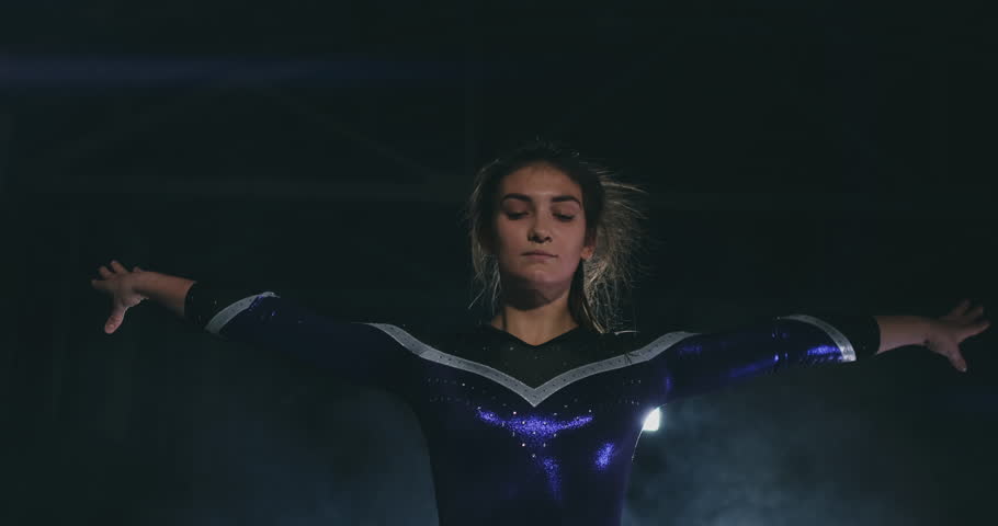 In slow motion in the smoke, a girl athlete stands with her arms raised after performing exercises. Welcome gesture with your hands.