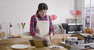 slow movement of young asian woman in apron preparing valentines day gift for boyfriend. wife at house modern wooden kitchen watching video online handmade chocolate process making cocoa dessert.