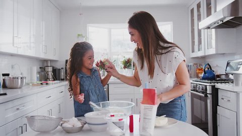 Mother and daughter preparing cake mix, tasting it and dabbing it on each other's noses, close up