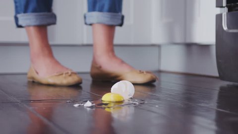 An egg falling to the kitchen floor and breaking on the wooden floorboards, low angle, slow motion