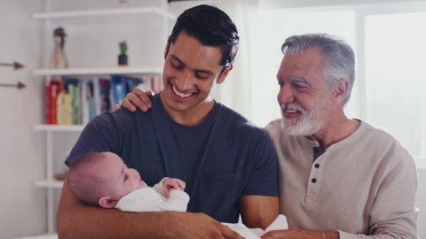 Proud Hispanic father holding his four month old son at home, with grandfather beside them, close up