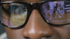 Macro shot of young black man in stylish black rim glasses having video conference with colleagues