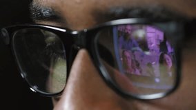 Extreme close up shot of concentrated young African man in black rim eyeglasses having video conference with colleagues