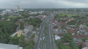 Aerial footage view drone flying backward of busy traffic cars and motorbike in curved outer ring road with shopping mall building background, Yogyakarta city, Indonesia