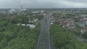 Aerial footage view drone flying backward of busy traffic in curved outer ring road with shopping mall building background, Yogyakarta city, Indonesia
