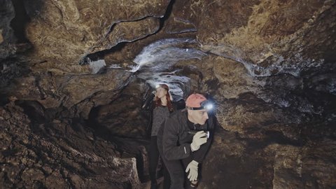 Group of men and women exploring an underground cave making their way along a rocky tunnel or shaft by the light of headlamps.