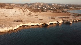 Video from the air. Video camera flies over the wild beach of Cyprus near Limassol. Rocky white beach, turquoise sea, underwater caves and village at dawn. Sunny morning.