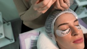 A close-up video of eyelash extension procedure. The artist fixes her client's eyelashes by applicating the new ones.