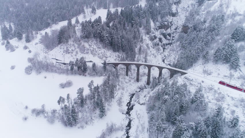 Viaduct and Train at Winter Day in Swiss Alps. Snowing. Switzerland. Aerial View. Drone Flies Forward and Downward Royalty-Free Stock Footage #1024700573