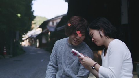 Young couple sitting outside and looking on the girlfriend's phone with emojis flying from phonein Kyoto, Japan. Close up to wide shot on 4k RED camera on a gimbal.
