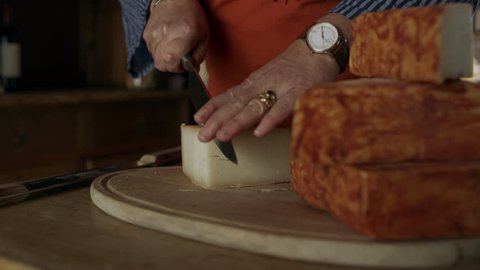 In a cheese shop, an Italian cheese maker cuts a block of cheese with a knife and tastes it. Medium shot on 8k helium RED camera.
