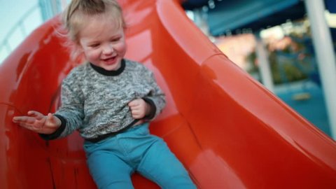 A young toddler laughs and enjoys the playground at a park as he slides down the slide.