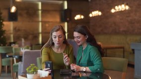 Two beautiful young women are sitting in a cafe and talking in a video chat by phone. Both women are absolutely calm and relaxed. The have a conversation with a client or business partner.