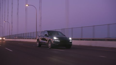 Portland, OR / USA Circa 2018 - Tracking shot of Porsche SUV driving on freeway bridge at dusk.