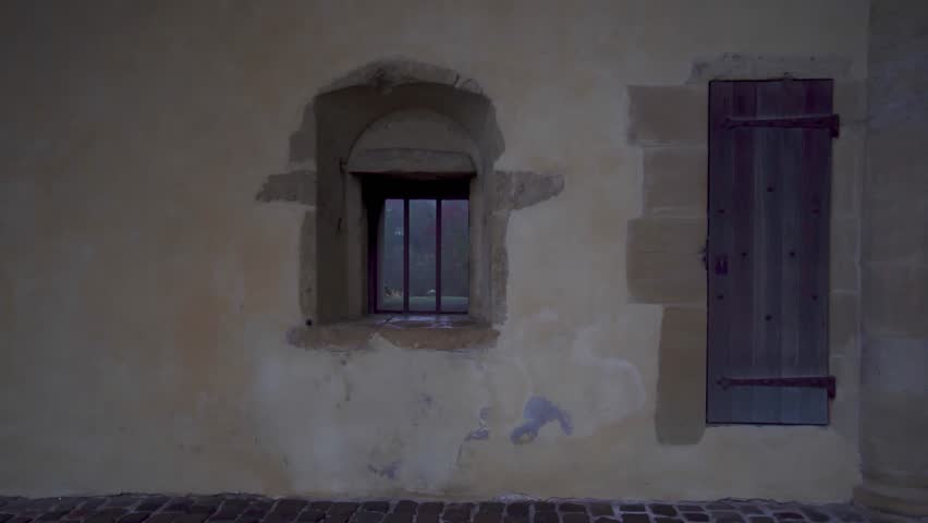 Girl passing Middle Ages fortification wall and stops by little window to take a look and enjoy the view