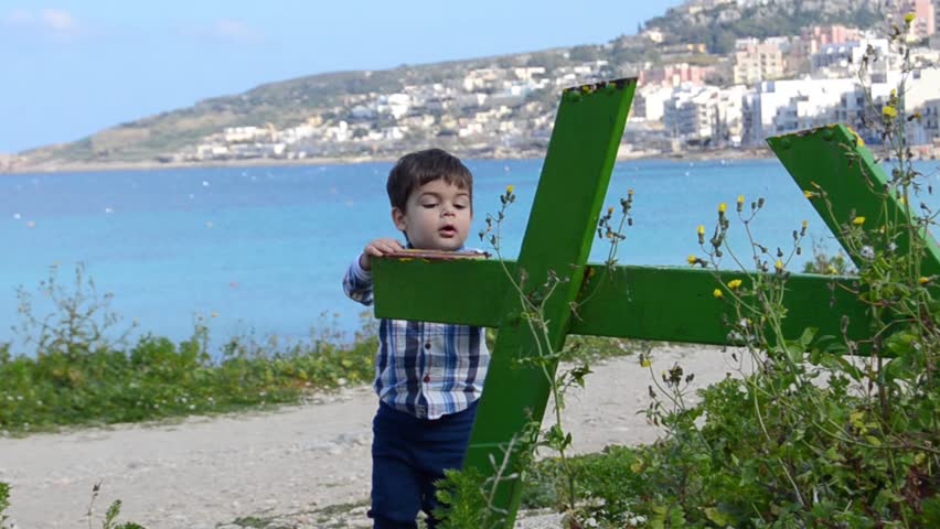 cute two years old baby boy climbing on green broken table in the park sea in the background.