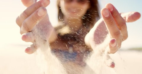 Close up of pretty girl pouring sand running through fingers slow motion at the beach with sun flare and blue skye REG DRAGON