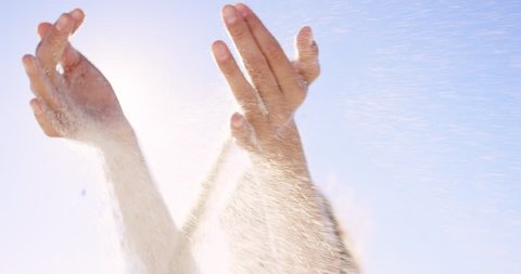 Close up of woman pouring sand running through fingers slow motion at the beach with sun flare and blue skye REG DRAGON