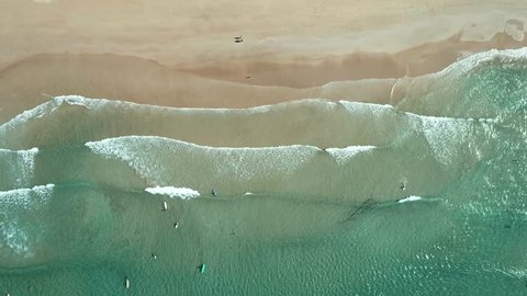 Top view of waves break on tropical white sand beach and surfers with surfing boards. Aerial drone view 4k shot of sea waves on the beautiful beach.