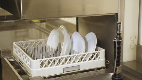 close up, white plate on basket in automatic dishwasher machine for industrial , dishwasher in the kitchen cafeteria, canteen, self-service restaurant. dishwashing process, plates are washed in the