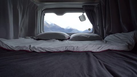 SLOWMO - Interior of motorhome bed with pillows and blankets by Lake Wakatipu, Queenstown, New Zealand with snowcapped mountains in background