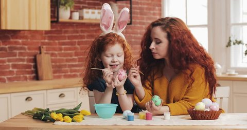 Happy easter. Mom and her little daughter are preparing for Easter. happy family painting Easter eggs in cozy kitchen. Little girl wearing bunny ears