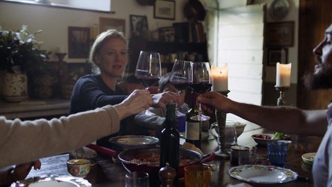While enjoying a family meal together, the adults raise their wine glasses to say 'cheers' and they enjoy their wine. Medium shot on 8k helium RED camera.