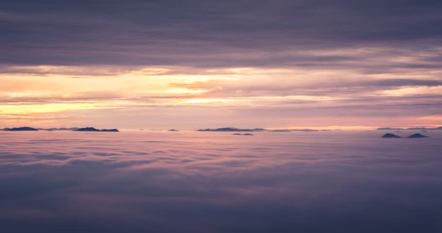 Sunrise over the Ljjubljana basin, with sea like moving fog covering it and the rising sun coloring the sky magenta and orange. Occasional hill can be seen outside of the fog.