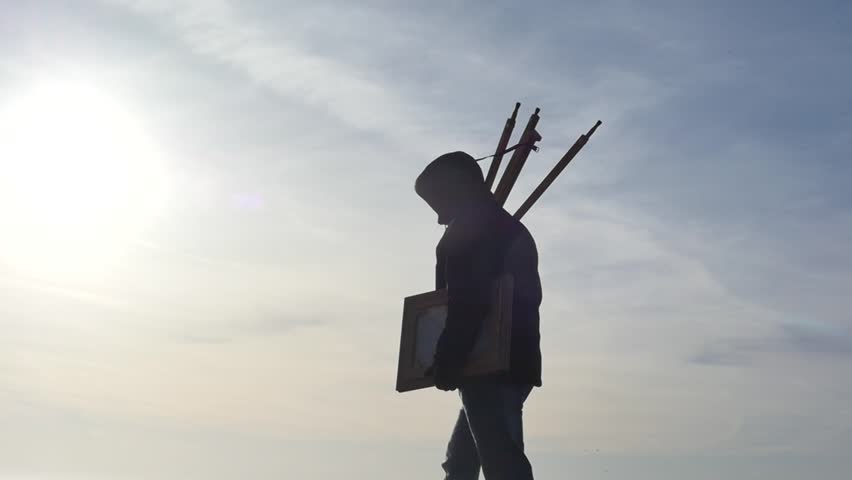 modern painter with easel & arwork in hands slow motion silhouette at stormy weather