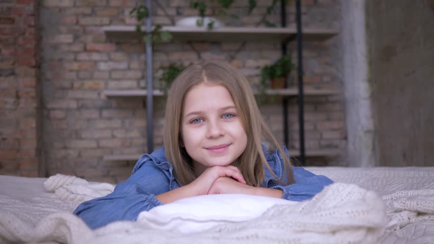 portrait of lovely child girl with blue eyes lying on pillow on bed in room at home