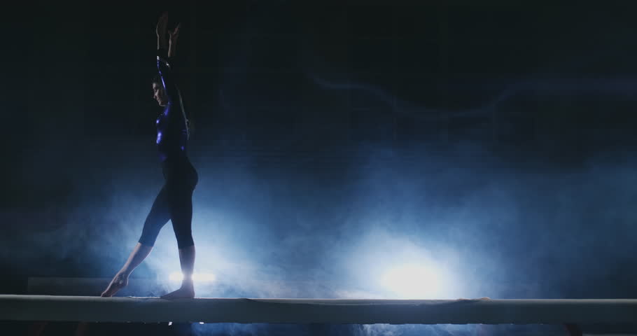 The girl is a professional athlete performs gymnastic acrobatic trick on a beam in backlight and slow motion in sports gymnastic clothing. Smoke and blue. Jump and spin on the balance beam Royalty-Free Stock Footage #1024774247