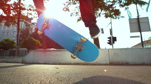 SLOW MOTION, CLOSE UP, LENS FLARE: Cool skateboarder riding through the city lands a fakie kickflip. Unrecognizable male skateboarder landing a difficult kickflip while enjoying his summer at the park