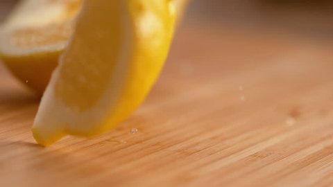 SLOW MOTION, DOF, MACRO: Fragrant bright yellow lemon quarters fall onto the wooden cutting board. Cinematic shot of sour lemon juice droplets splashing as sliced lemon falls on the kitchen table.